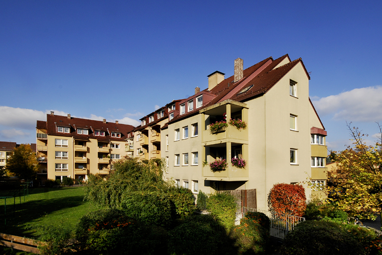 Mehrfamilienhaus mit Balkonen und Blumenkästen, herbstlicher Vorgarten mit Strauchbepflanzung