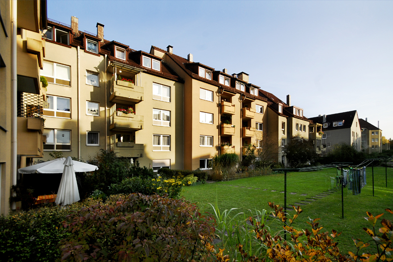 Mehrfamilienhäuser mit gelber Fassade und Balkonen, Blick in den begrünten Innenhof mit Rasenfläche und Sonnenschirm