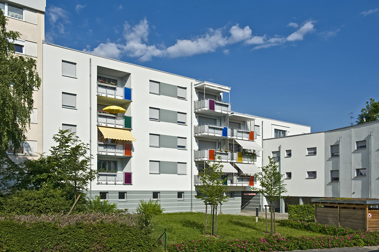 Mehrfamilienhaus in der Kachletstraße 8 in Nürnberg, Frontansicht mit bunten Balkonen und Markisen, Vorgarten mit jungen Bäumen