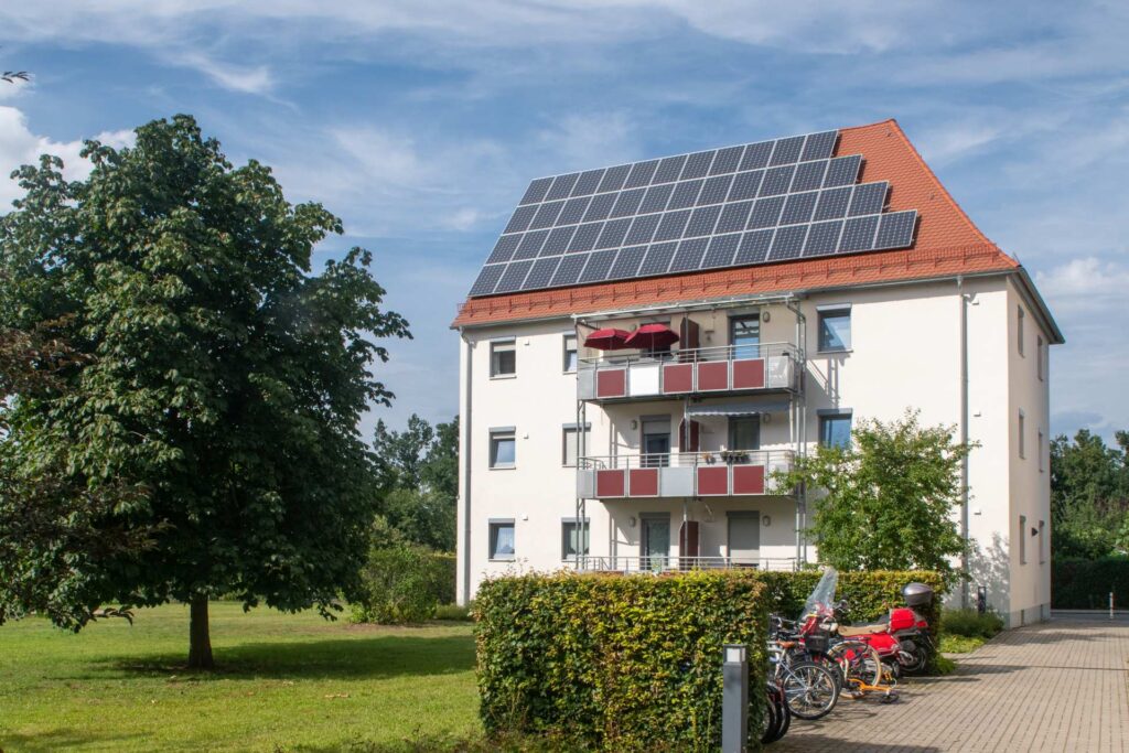 Wohngebäude mit dunkelroten Balkonen und Solaranlage auf dem Dach, im Vordergrund Fahrräder und Bäume