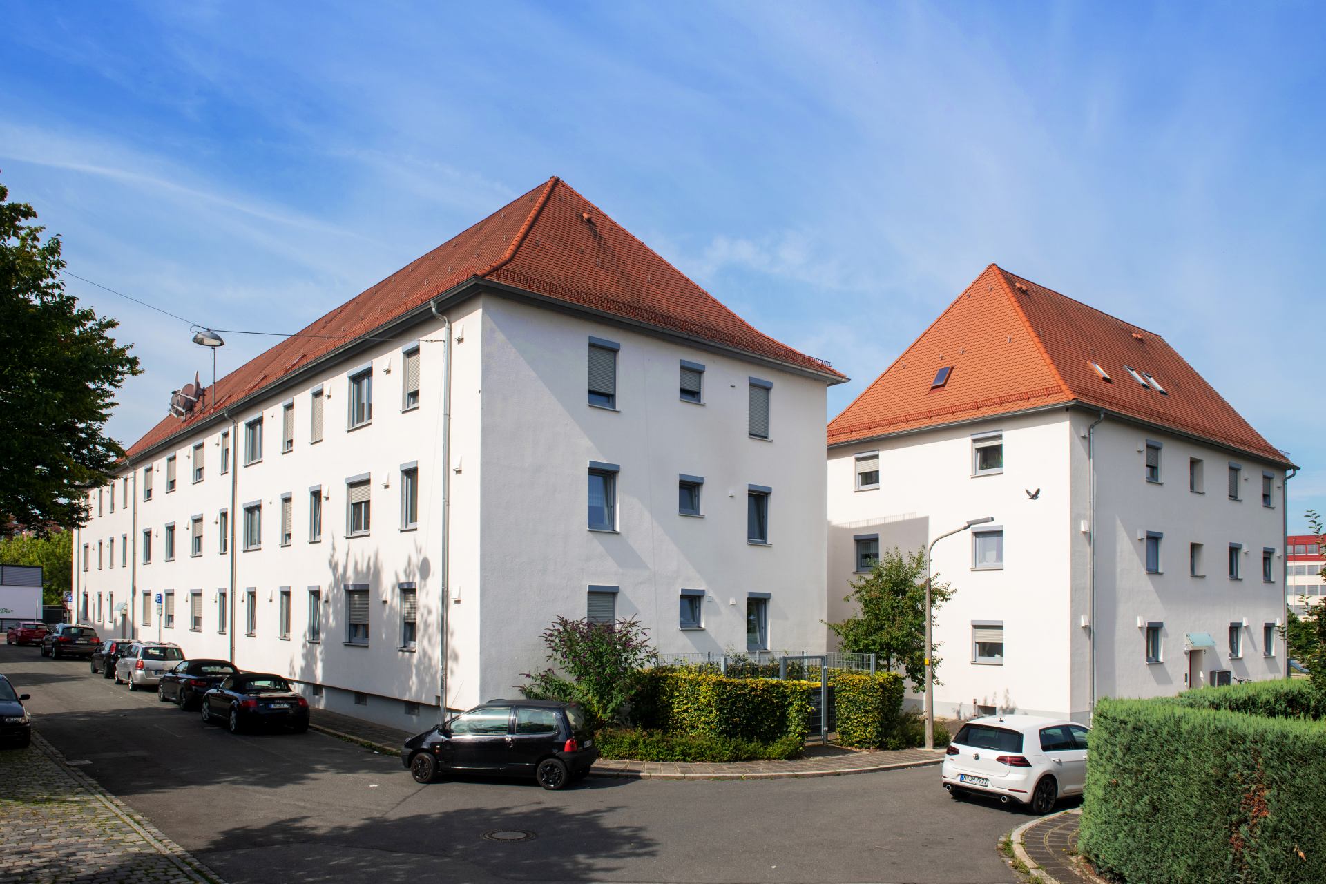 Weiße mehrstöckige Wohngebäude mit rotem Satteldach, Straßenansicht mit parkenden Autos