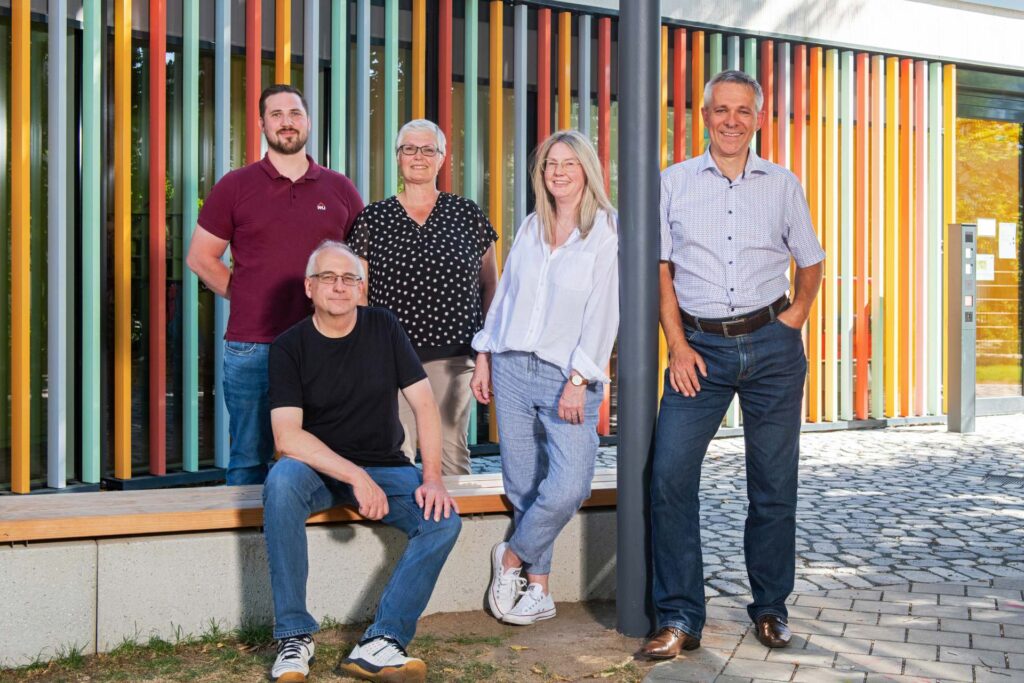 Gruppenfoto von fünf Personen vor einer bunt gestreiften Fassade im Freien