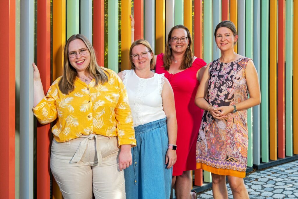 Gruppenfoto von vier Frauen vor einer bunt gestreiften Wand
