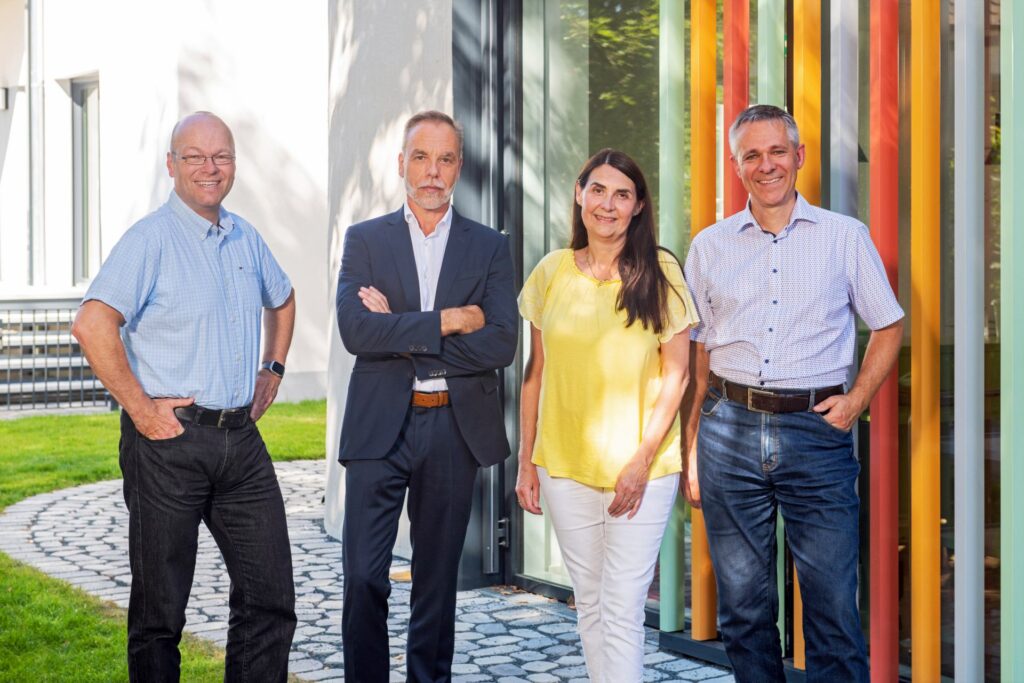 Gruppenfoto von vier Personen vor dem Eingang eines Gebäudes mit bunt gestreifter Fassade