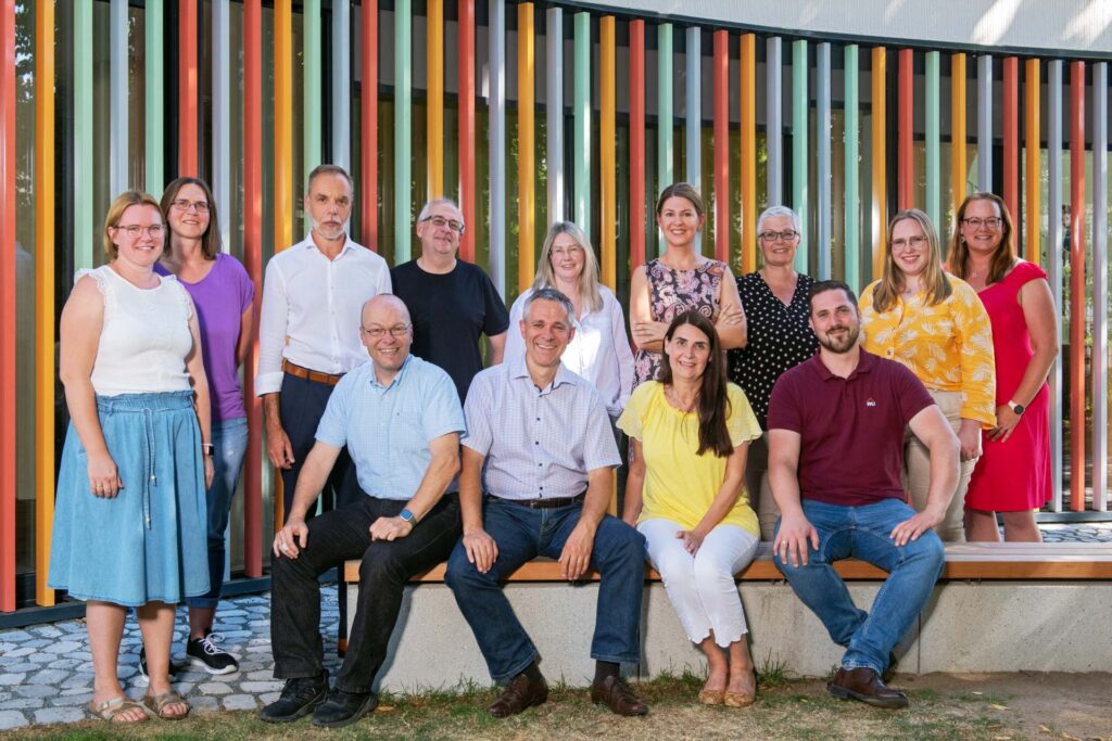 Gruppenfoto eines Mitarbeiterteams vor einer bunt gestreiften Wand im Freien